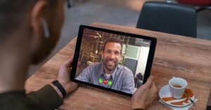 Homem sentado à mesa utilizando um tablet para fazer videochamada